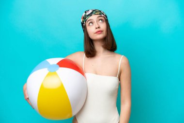 Elinde plaj topu tutan genç Ukraynalı kadın mavi arka planda izole edilmiş ve yukarı bakıyor.