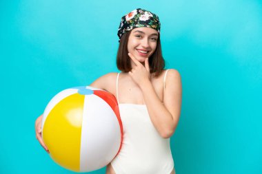Young Ukrainian woman holding beach ball isolated on blue background happy and smiling