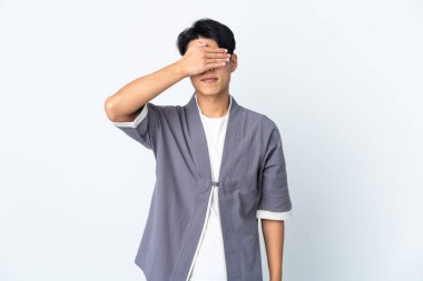 Genç Çinli bir adam beyaz arka planda izole edilmiş, gözleri elle kapatıyor. Bir şey görmek istemiyorum.
