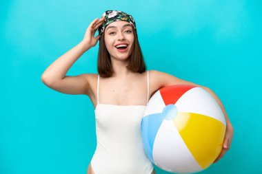 Elinde plaj topu tutan genç Ukraynalı kadın mavi arka planda, sürpriz bir ifadeyle izole edilmiş.