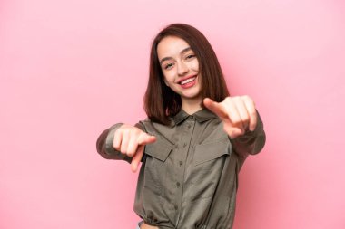 Pembe arka planda izole edilmiş genç Ukraynalı kadın mutlu bir ifadeyle ön tarafı işaret ediyor