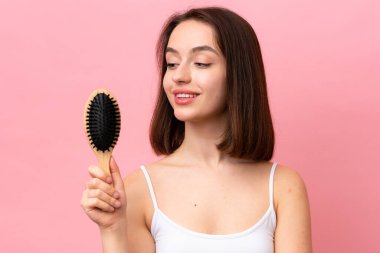 Young Ukrainian woman isolated on pink background with hair comb and looking it