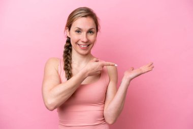 Pembe arka planda izole edilmiş genç beyaz kadın bir ilan vermek için avucunun içinde hayali bir fotokopi makinesi tutuyor.