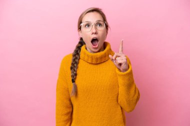 Pembe arka planda izole edilmiş genç beyaz bir kadın, bir fikrin işaret ettiğini düşünüyor.