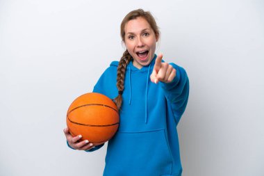 Beyaz arka planda izole edilmiş basketbol oynayan beyaz kadın şaşırmış ve ön tarafı işaret ediyor.