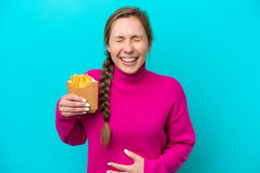 Genç beyaz kadın elinde kızarmış cipslerle mavi arka planda izole edilmiş gülümsüyor.