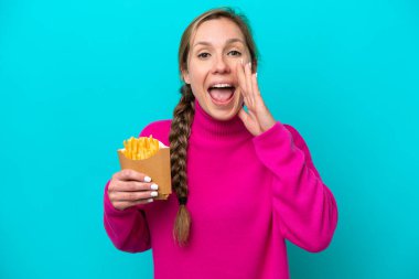 Elinde kızarmış cips tutan beyaz bir kadın mavi arka planda izole edilmiş ve ağzı açık bağırıyor.