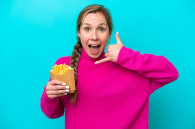 Mavi arka planda izole edilmiş kızarmış cips tutan beyaz bir kadın telefon jesti yapıyor. Bana geri dönüş işareti ver.