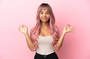 Pembe saçlı melez kadın pembe arka planda Zen pozisyonunda.