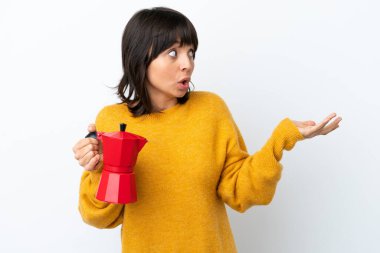 Beyaz arka planda kahve demliği tutan melez bir kadın. Sürpriz bir ifadeyle yan yana bakarken.