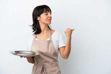 Tepsisi beyaz arkaplanlı genç garson bir ürünü sunmak için kenarı işaret ediyor.