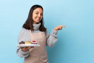 Pasta şefi izole edilmiş mavi arka planda büyük bir pasta tutuyor..