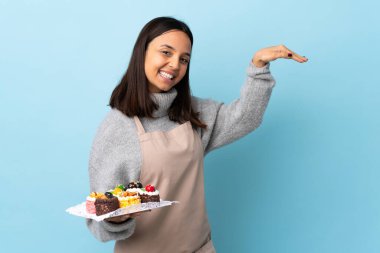 Pasta şefi, izole edilmiş mavi arka plan üzerinde büyük bir pasta tutuyor. Reklam koymak için kopyalama alanı tutuyor..