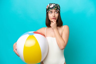 Plaj topu tutan genç Ukraynalı kadın mavi arka planda izole edilmiş şüpheleri ve düşünceleri var.