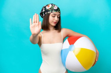 Young Ukrainian woman holding beach ball isolated on blue background making stop gesture and disappointed