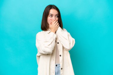 Genç Ukraynalı bir kadın mavi arka planda izole edilmiş ağzını kapatıyor ve yan tarafa bakıyor.
