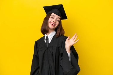 Young university graduate Ukrainian woman isolated on yellow background saluting with hand with happy expression