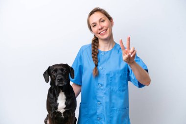 Beyaz arka planda izole edilmiş köpekli genç bir veteriner kadın gülümsüyor ve zafer işareti gösteriyor.