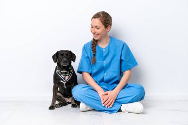 Köpeğiyle yerde oturan genç veteriner kadın mutlu bir ifadeyle beyaz arka planda izole edilmiş.