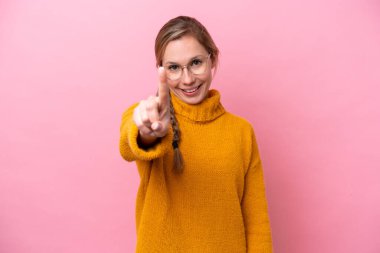 Pembe arka planda izole edilmiş genç beyaz kadın parmağını kaldırıyor ve gösteriyor.