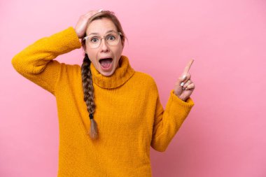 Pembe arka planda izole edilmiş beyaz bir kadın. Şaşırmış ve işaret ediyor.