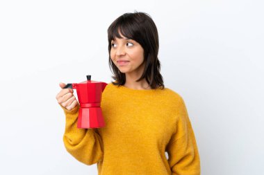 Young mixed race woman holding coffee pot isolated on white background looking side