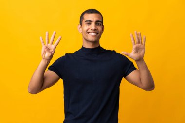 İzole edilmiş sarı arka planda sayıları sayan Afrikalı Amerikalı bir adam.