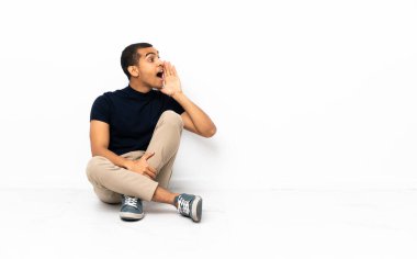 Afro-Amerikalı bir adam yerde oturmuş ağzı sonuna kadar açık bağırıyor.