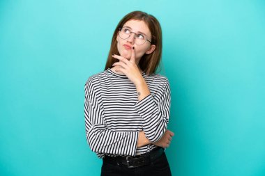 Mavi arka planda izole edilmiş genç bir İngiliz kadın yukarı bakarken şüphe duyuyor.