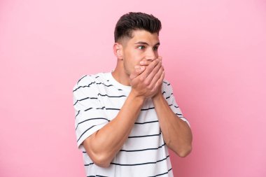 Pembe arka planda izole edilmiş genç beyaz adam ağzını kapatıyor ve yan tarafa bakıyor.