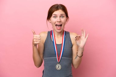 Pembe arka planda madalyaları olan genç bir İngiliz kadın tamam işareti ve baş parmak hareketi gösteriyor.