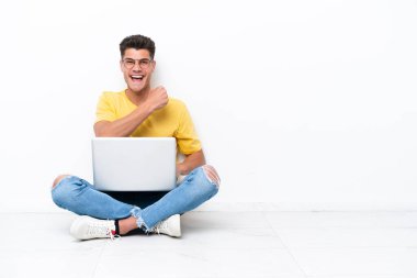 Young man sitting on the floor isolated on white background celebrating a victory