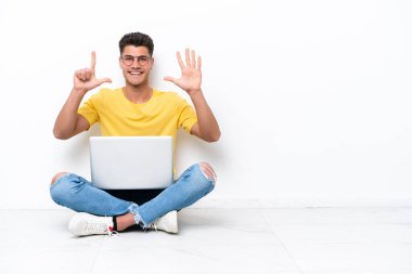 Young man sitting on the floor isolated on white background counting seven with fingers
