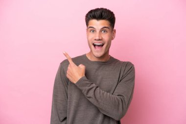 Pembe arka planda izole edilmiş genç beyaz adam şaşırmış ve işaret ediyor.