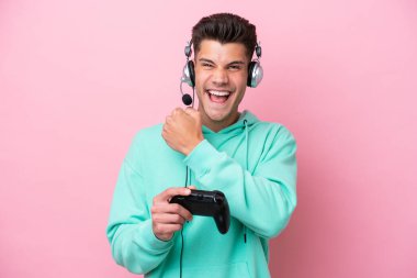 Pembe arka planda izole edilmiş bilgisayar oyunu kontrolörüyle oynayan yakışıklı beyaz bir adam zaferi kutluyor.