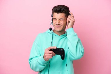 Pembe arka planda izole edilmiş bir bilgisayar oyunu kontrolörüyle oynayan yakışıklı beyaz adam hayal kırıklığına uğramış ve kulaklarını tıkamış.