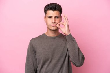 Pembe arka planda izole edilmiş genç beyaz adam sessizlik işareti gösteriyor.