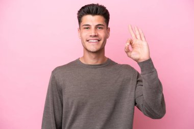 Pembe arka planda izole edilmiş genç beyaz adam parmaklarıyla tamam işareti gösteriyor.