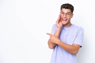 Beyaz arka planda izole edilmiş genç beyaz bir adam bir ürün sunmak ve bir şeyler fısıldamak için kenarı işaret ediyor.