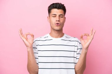Zen pozisyonunda pembe arka planda izole edilmiş genç beyaz bir adam.