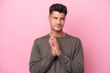 Pembe arka planda izole edilmiş genç beyaz bir adam bir şeyler planlıyor.