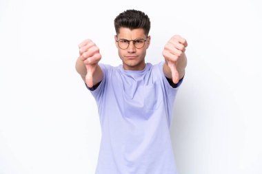 Beyaz arka planda izole edilmiş genç beyaz bir adam baş parmağını iki eliyle aşağı gösteriyor.