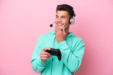 Pembe arka planda izole edilmiş bir bilgisayar oyunu kontrolörüyle oynayan yakışıklı beyaz adam gülümserken yukarı bakıyor.