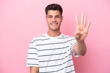 Pembe arka planda izole edilmiş genç beyaz adam mutlu ve parmaklarıyla dört tane sayıyor.
