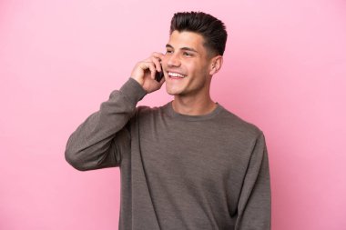 Pembe arka planda izole edilmiş genç beyaz adam cep telefonuyla sohbet ediyor.