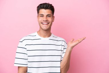 Pembe arka planda izole edilmiş genç beyaz bir adam bir ilan vermek için avucunun içinde hayali bir fotokopi makinesi tutuyor.