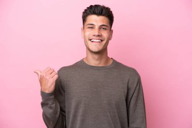 Pembe arka planda izole edilmiş genç beyaz adam bir ürünü sunmak için kenarı işaret ediyor.