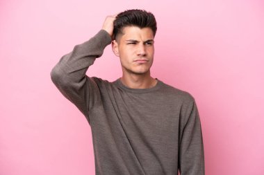 Kafkasyalı genç bir adam pembe arka planda izole edilmiş, kafası kaşınırken şüpheleri var.