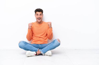 Yerde tek başına oturan genç adam, beyaz arka planda zaferi kutluyor.