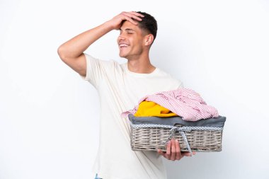 Çamaşır sepetini tutan beyaz arka planda izole edilmiş genç beyaz bir adam çok gülümsüyor.
